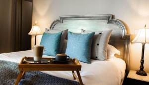 Una cama con almohadas azules y una bandeja con tazas. en Elephant Hotel en Pangbourne