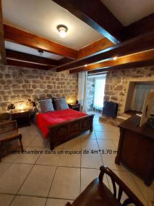 a bedroom with a red bed and a stone wall at La Grange de La Coste in Saint-Barthélemy-le-Meil
