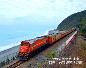 an orange train traveling down the tracks near the ocean at 童趣漫旅溜滑梯民宿 可預約包棟 in Taitung City