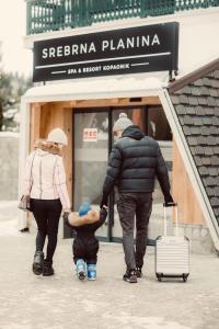 a man and woman walking down a street with a child and a suitcase at SREBRNA PLANINA Spa & Resort in Kopaonik