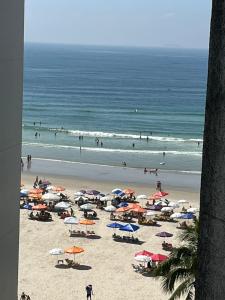 une plage avec de nombreux parasols et des gens dans l'océan dans l'établissement APARTAMENTO NA RUA DA PRAIA COM VISTA PARA O MAR, à Guarujá
