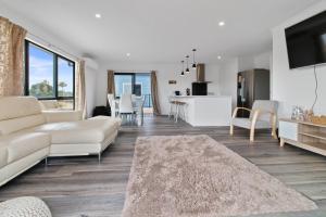 a living room with a white couch and a kitchen at Sandy Shores - Waihi Beach Holiday Home in Waihi Beach