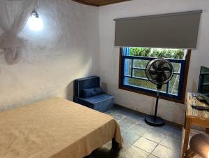 Schlafzimmer mit einem Bett, einem Ventilator und einem Fenster in der Unterkunft Chalés Bambá in Ilhabela