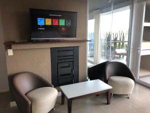 sala de estar con 2 sillas y chimenea con TV en Linda Bay spa playa Unidad 603 Mar de Las Pampas, en Mar de las Pampas