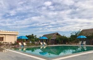 a swimming pool with blue umbrellas and chairs at E-Outfitting Royal Inn Bagan in Myene