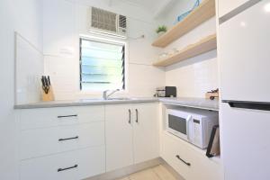 eine Küche mit weißen Schränken, einem Waschbecken und einem Fenster in der Unterkunft Amaroo On Mandalay in Nelly Bay