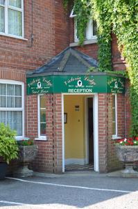 a red brick building with a green and white reception sign at Victoria Lodge Guest House in Salisbury