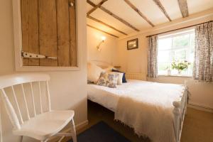 a bedroom with a bed and a chair and a window at Spadgers, a flax workers cottage next to fields in a Medieval Village in Long Melford