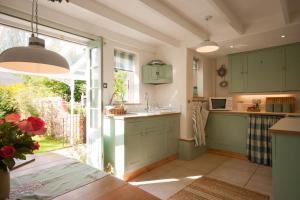 a kitchen with green cabinets and a large window at Romney, a cosy Victorian cottage in a picturesque Suffolk village in Cavendish