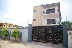 ein weißes Haus mit einem schwarzen Tor und zwei Bäumen in der Unterkunft Captivating 2-Bed Ensuite Apartment in Accra in Accra