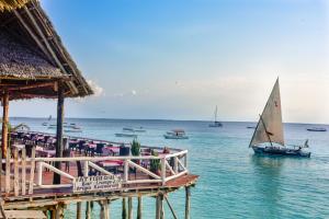 a sail boat in the water next to a restaurant at Amaan Beach Bungalows in Nungwi