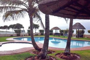 a swimming pool with two palm trees in a resort at Inyoni Rocks Cabanas No 40 in Amanzimtoti