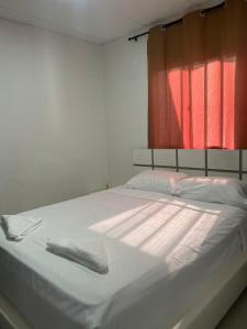 Una cama con sábanas blancas y una ventana roja. en Apartamento Ucha, en Ríohacha