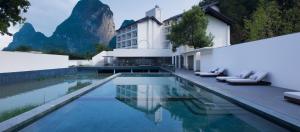 阳朔Guilin Yangshuo Nine Roots Luxury Hotel的一家带游泳池的酒店，背景是一座山