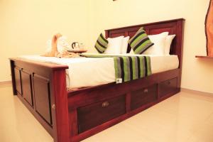 Cama grande de madera con sábanas blancas y almohadas verdes en Odani Villa, en Weligama