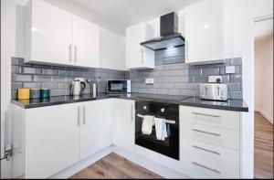 uma cozinha com armários brancos e electrodomésticos pretos em 4 Bed Executive Style House - Near City Centre em Swansea