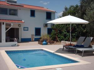 a swimming pool with an umbrella and chairs and a house at vivenda descollaz in Falcoeiras