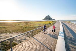 two people riding bikes on a sidewalk next to the beach at Cottage Le Phare in Mont-Dol
