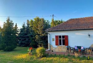 ein weißes Haus mit einem roten Fenster und Stühlen in der Unterkunft Tiszai Fenyves Apartman in Tiszadorogma