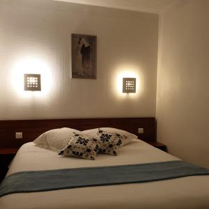 a bed with two pillows and two lights on the wall at Hotel Restaurant Les Oceanides in Concarneau