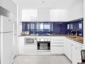 una cocina blanca con armarios y electrodomésticos blancos en Circle on Cavill 25th Floor with Ocean Views, en Gold Coast