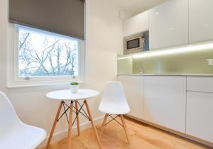 a kitchen with white cabinets and a table and two chairs at Shepherds Bush Green Serviced Apartments by Concept Apartments in London