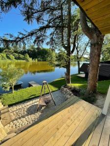 a wooden deck with a swing next to a lake at Hyggelig sommerhus. med udsigt, til vand fra senge in Veksø
