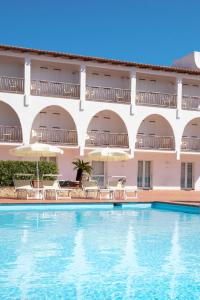 una piscina frente a un hotel con sillas y sombrillas en Club Hotel Cormorano, en Baja Sardinia