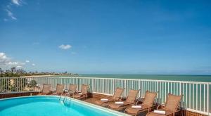 a balcony with a swimming pool and chairs and the ocean at Happy Hotel Manaíra in João Pessoa