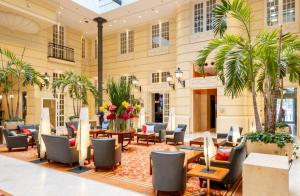a lobby with chairs and tables and palm trees at Hotel Polonia Palace in Warsaw