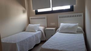 a bedroom with two beds with white sheets and a window at Casa La Palmera - Sólo Familias y Parejas in Conil de la Frontera