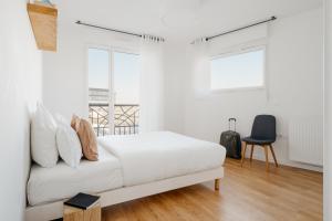 a white bedroom with a bed and a chair at Edgar Suites Levallois – Jules Verne in Levallois-Perret
