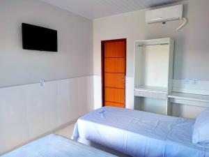 a white room with a bed and a television at Pousada Portal da Villa in Vitória da Conquista