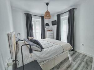 a white bedroom with a bed and two windows at ARTE Playa la Caleta Grupo AC Gestion in Cádiz