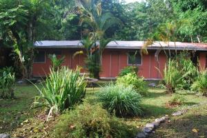 una casa roja en medio de un jardín en Los Mineros Guesthouse, en Dos Brazos