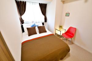 1 dormitorio con 1 cama y 1 silla roja en はなハウス 2F en Ginowan