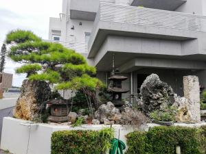 a garden in front of a building with a pine tree at Room Biotop YOMITAN in Yomitan
