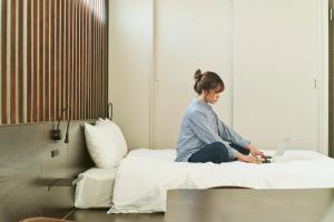 a woman sitting on a bed with a laptop at FAV HOTEL TAKAMATSU in Takamatsu
