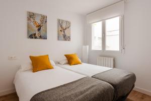 two beds in a white room with two orange pillows at Apartamento Nuevo Centro Granada in Granada