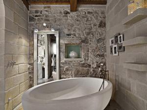 baño con bañera blanca grande y pared de piedra. en Relais Masseria Capasa, en Martano