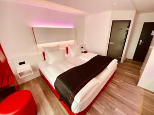 Schlafzimmer mit einem großen weißen Bett mit roten Akzenten in der Unterkunft DORMERO Hotel Bretten in Bretten