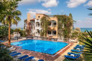 uma piscina em frente a um edifício com cadeiras e o oceano em Iliostasi Beach Apartments em Hersonissos