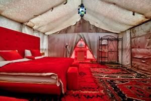 a bedroom with a red bed with a red bedspread at Camel Desert Camp in Merzouga +19 photos