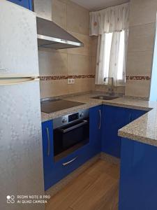 a small kitchen with blue cabinets and a refrigerator at APARTAMENTO EN ROMPIDO con piscina, chiringuito y pistas in Huelva