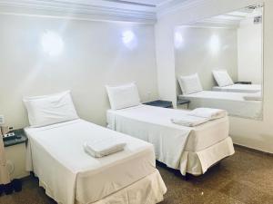 Duas camas num quarto branco com um espelho. em Hotel Sol Buriti em Goiânia