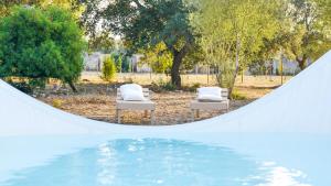twee witte ligstoelen naast een zwembad met water bij Cuturi Wine Glamping in Manduria