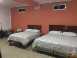 2 Betten in einem Zimmer mit orangefarbener Wand in der Unterkunft Casa alebrijes in San Agustin de las Juntas