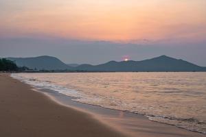 a beach at sunset with the ocean and mountains at RimLay Beachfront Pool Villa in Sattahip