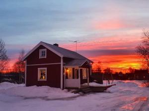 uma pequena casa na neve com um pôr-do-sol ao fundo em Guesthouse em Öjebyn