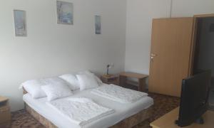 a bedroom with a bed with white sheets and a television at Jartó Apartman in Harkány